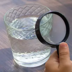 Une main tient une loupe pour analyser l'eau d'un puits dans un verre.