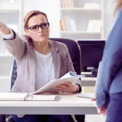 Szefowa wskazuje palcem na drzwi, sugerując pracownikowi, że jego nieobecność usprawiedliwiona niepłatna dobiegła końca.