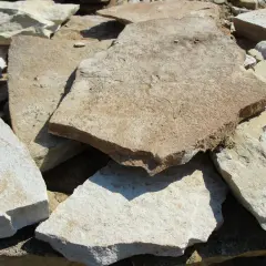 Stosy nierównych, płaskich kamieni piaskowiec w odcieniach beżu i bieli, gotowe do budowy ścieżki.
