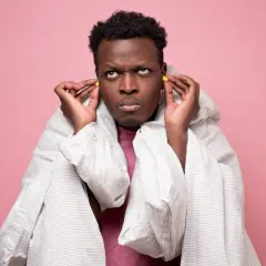 Homme frustré met des bouchons d'oreilles, enveloppé dans une couette. Il prépare sa lettre de nuisance sonore au maire.