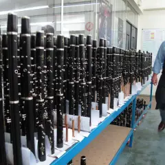 Un homme en tablier inspecte un buffet de clarinettes, prêt à être expédié. Ces instruments de musique, des modèles "crampon mantes", sont alignés sur des étagères.