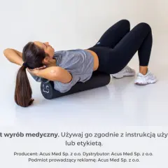 Kobieta z rękami za głową na wałku do masażu, rozluźnia spięte mięśnie pleców.