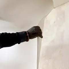 Un ouvrier pose de la fibre de verre dans les angles d'un mur.