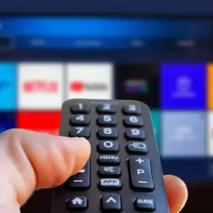 Hand håller fjärrkontroll framför en TV-skärm med app-ikoner. Kanske dags att välja en film eller en dokumentär om ze rappare.