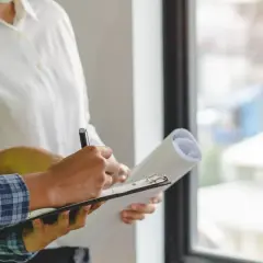 Un ouvrier en gilet jaune écrit sur un bloc-notes, tenant un rouleau de plans. Il s'agit d'une lettre de remboursement d'acompte pour des travaux non faits.