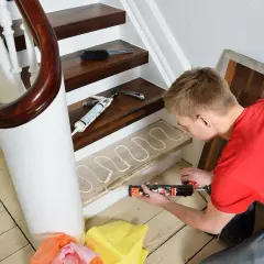 Man renoverar trappa med fogpistol och lim på en trappsteg.