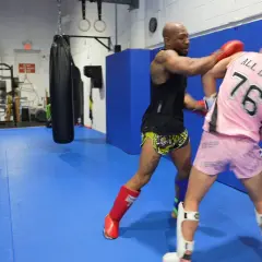 Two fighters practice boxing head movement drills in a gym. One throws a punch while the other dodges.