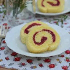Dwa kawałki biszkoptowego rolady z malinową żelką z galaretką na talerzyku, obok ozdobiony widelec.