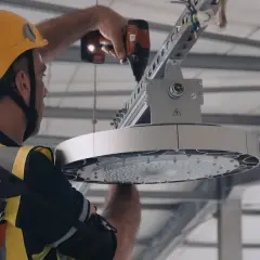 Pracownik w żółtym kasku i kamizelce montuje nowoczesne oświetlenie LED. To wymiana oświetlenia na LED – remont czy modernizacja hali.