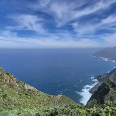 Vista del Roque de Tábarno, un promontorio verde y rocoso que se adentra en el mar azul bajo un cielo nublado.