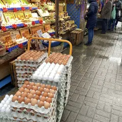 Duże stosy jajek na targu. Widać różne rodzaje i kolory, a także ceny.