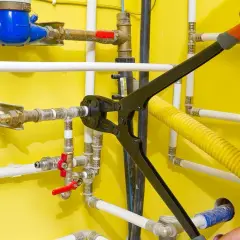 Instalator pokazuje, jak łączyć rury PEX za pomocą praski. Widać wodomierz i zawory.