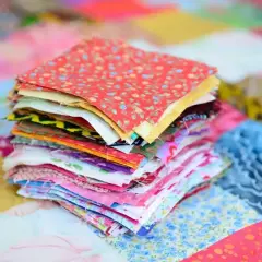 Stos kolorowych kwadratów materiałów, gotowych do stworzenia patchworku. To właśnie patchwork – sztuka łączenia skrawków tkanin w piękne wzory.