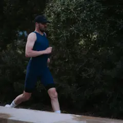 Mann in dunkelblauem Triathlonanzug läuft vor dunklem Grün.