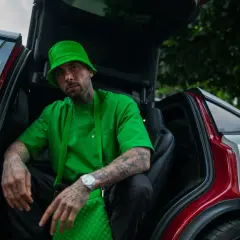 Malik Montana w zielonym kapeluszu i koszulce, siedzi w samochodzie z otwartymi drzwiami. Wygląda jak adwokat diabła, gotowy na nowe wyzwania.