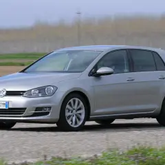Volkswagen Golf 1.6 TDI argento in movimento su strada sterrata, con campi coltivati sullo sfondo.