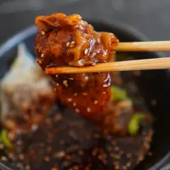 Chrupiące ciasto wonton w sosie, podniesione pałeczkami, posypane sezamem. Pyszna przekąska.