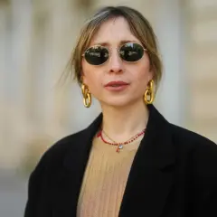 Frau mit stylischer curtain bangs frisur, runden Sonnenbrillen und auffälligem Goldschmuck.