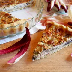 Una fetta di torta salata con taleggio, ricca e dorata, accanto a foglie di radicchio e prosciutto crudo.