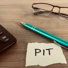 Kalkulator, zielony długopis i okulary leżą obok kartki z napisem PIT. Czas rozliczyć PIT 36L.