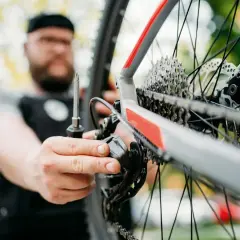 Mężczyzna z brodą dokręca śruby w przerzutce rowerowej. Dbałość o detale podczas tych momentów dokręcania śrub w rowerze zapewnia płynną jazdę.