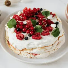 Pavlova z kremem do bezy, ozdobiona świeżymi malinami, borówkami i porzeczkami.