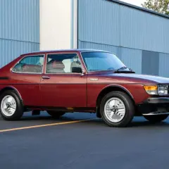 En röd Saab 99 Turbo står parkerad framför en blå hangar.