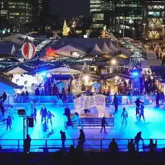 Patinage sur glace et marchés de Noël ouverts, illuminés par des lumières bleues vives. Une scène festive avec des chalets et des décorations scintillantes.