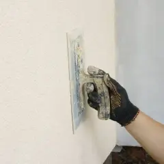 Ręka w rękawicy wygładza tynk, tworząc piękną strukturę elewacyjną.
