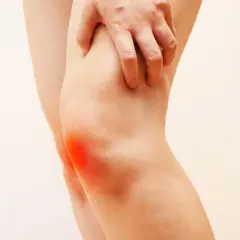 Mano che preme sul ginocchio con un'area rossa che indica dolore al ginocchio a letto.
