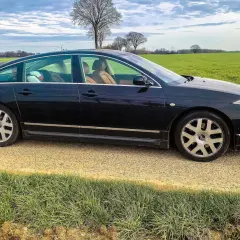 Ciemny Citroën C6 z beżowym wnętrzem stoi na żwirowej drodze obok zielonego pola.