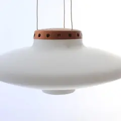 En vit, svävande ufo lampa med en trädetalj upptill.