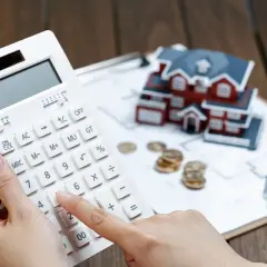 Calculadora en mano, se evalúa cuánto se deduce por alquiler de vivienda, con una maqueta de casa, monedas y planos.