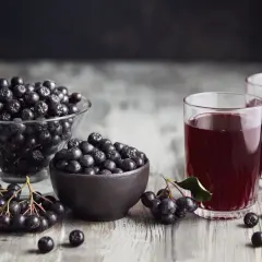 Szklanki z ciemnym sokiem i miseczki pełne aronii, gotowe na nalewkę z aronii.