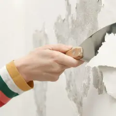 Mano con spatola che rimuove vernice a smalto scrostata dal muro.