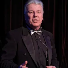 Emilian Kamiński w czarnym smokingu z muszką, jakby opowiadał o swoich filmach.