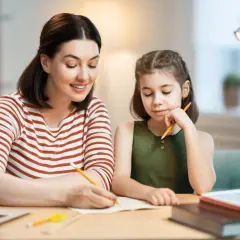 Mama pomaga córce w nauczaniu domowym podstawówka. Razem piszą w zeszycie, obok leży laptop.