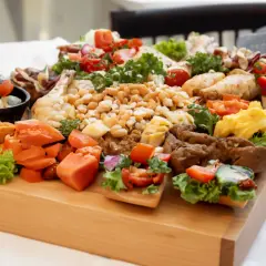 Bogato zastawione patery z przekąskami: mini kanapeczki z warzywami, jajecznica, kawałki kurczaka i inne smakołyki na drewnianej desce.