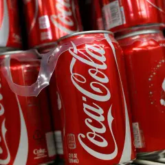Puszki Coca-Coli ułożone na półce, jedna z nich z widoczną etykietą kaloryczną.
