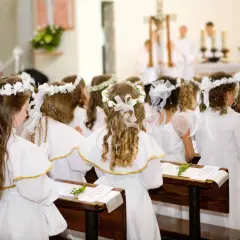 Dzieci w białych strojach, z wiankami na głowach, siedzą w ławkach kościoła. To uroczysty biały tydzień, czas pierwszej komunii świętej.