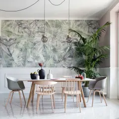 Un soggiorno moderno con carta da parati a tema tropicale, un tavolo da pranzo con sedie in legno e un'elegante cucina grigia. Chi mette la carta da parati sceglie un tocco di natura.