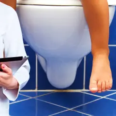 Medico con tablet osserva bambino sul water. Possibile problema di cacca bianca bambini.