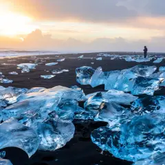 Fragmentos de hielo brillan en la arena negra del Diamond Beach de Islandia, bajo un cielo crepuscular.