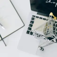 Miniaturowy wózek na zakupy z paczką na klawiaturze laptopa. Obok notatnik z długopisem. Symbolizuje sytuację, gdy klient nie odebrał opłaconej przesyłki.