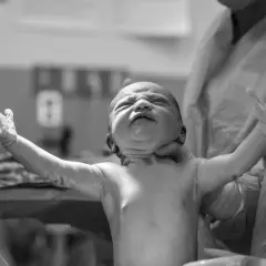 Neonato con movimenti a scatti delle braccia, appena nato, con espressione intensa e occhi chiusi.