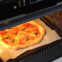 Une pizza maison dorée et appétissante est en pleine cuisson dans un four moderne. Le fromage fond et les herbes parfument l'air.