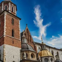 Kraków: Wawel z ceglaną wieżą, złotą kopułą i zielonym dachem pod błękitnym niebem.