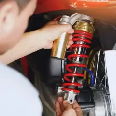 Mechanik dokonuje wymiany amortyzatorów w skuterze, używając złotego narzędzia do regulacji.