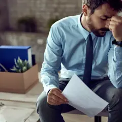 Homme stressé tenant une lettre de plainte au syndic de copropriété, avec une boîte de déménagement derrière lui.