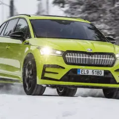 En ljusgrön Skoda Enyaq testas i snö. Bilen kör genom ett vinterlandskap med träd i bakgrunden.